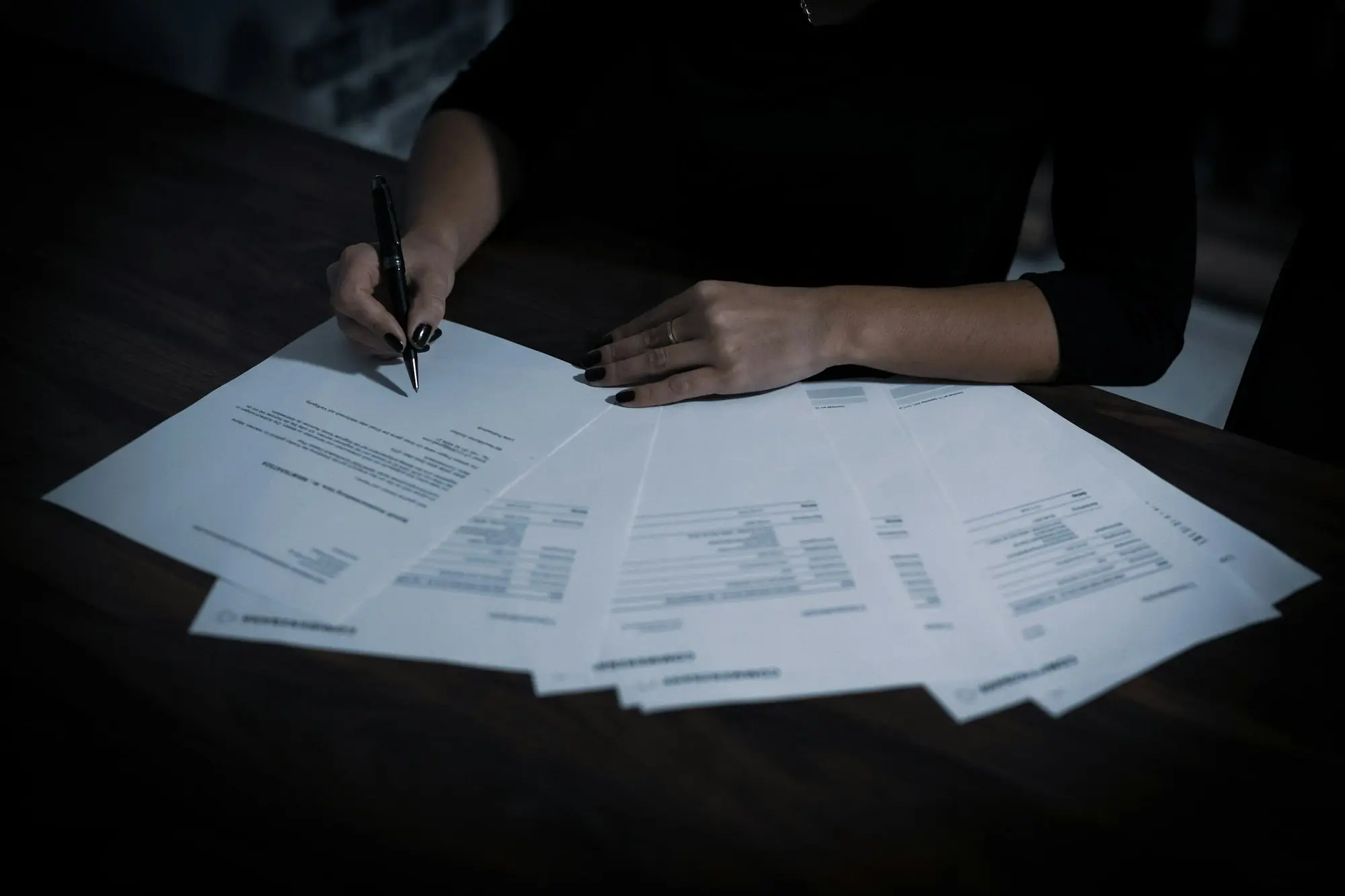 Person reviewing and signing a spread of printed documents