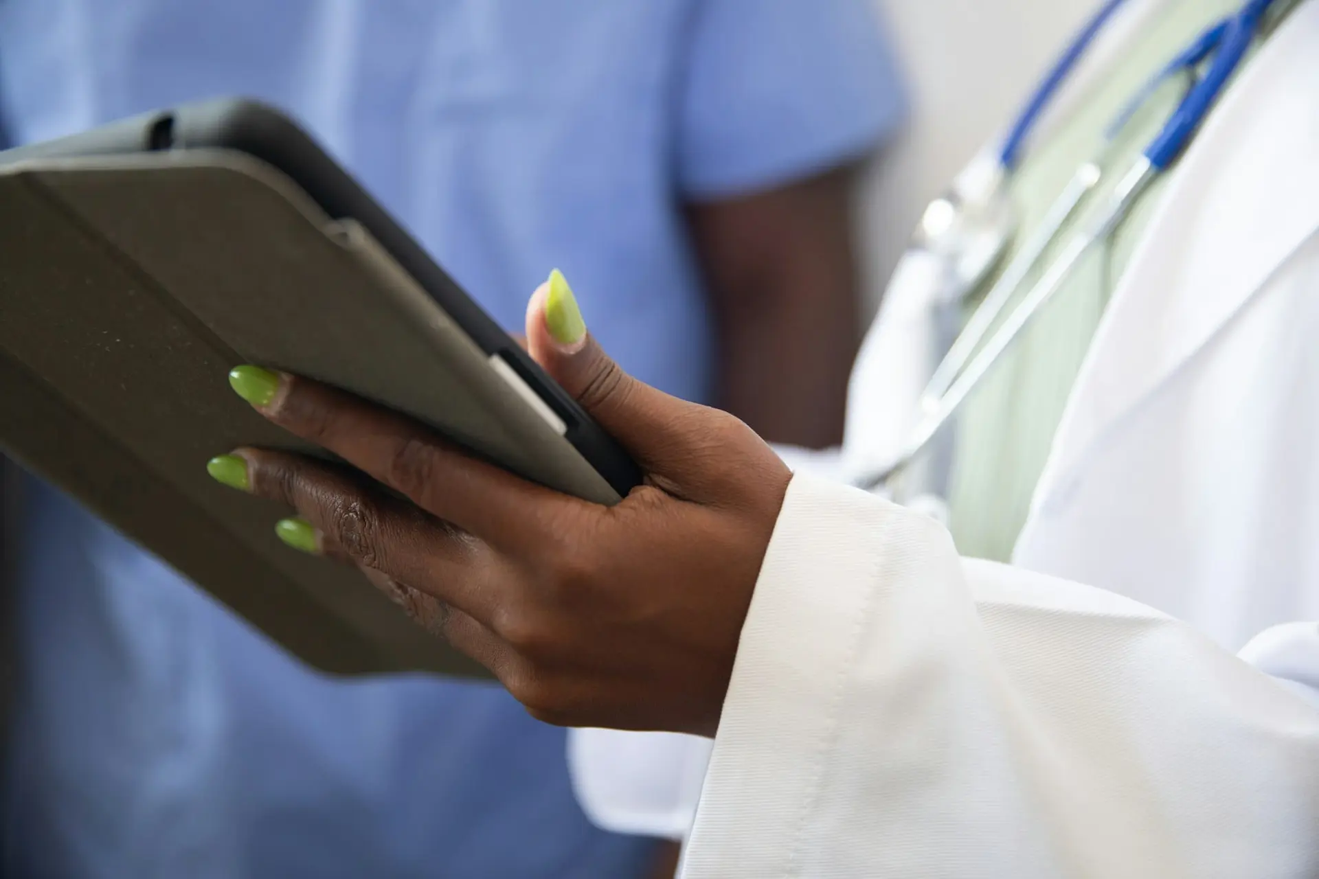 Clinician in a white coat and stethoscope holding a tablet