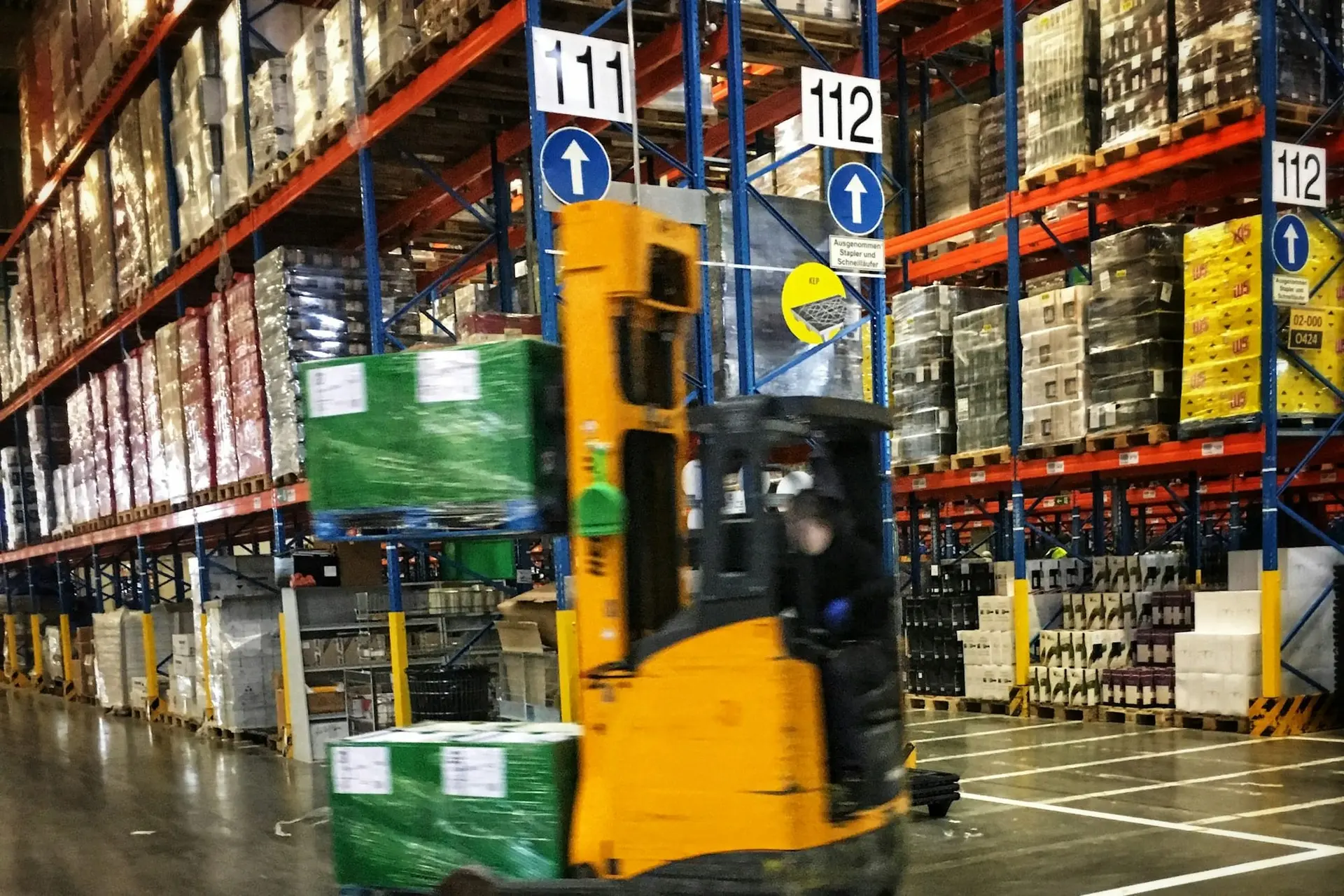 Forklift moving pallets between tall racks in a warehouse